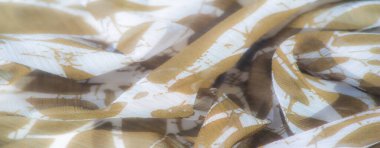 Açık kahverengi kumaşın detaylı bir görüntüsü ve yapraklara benzeyen beyaz soyut desenler. Kumaşlar pürüzsüz doku ve nazik kıvrımlar zarif ve doğal bir akış sağlar..