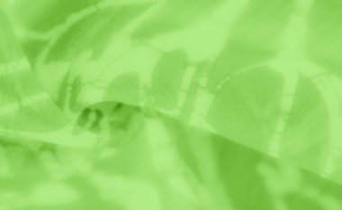 Yeşil kumaştan bir yakın çekim, karmaşık desenlerini ve yumuşak kıvrımlarını vurguluyor. Görüntü, ışık dengesi ile soyut, rahatlatıcı bir görsel sunar.