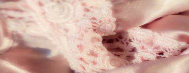 İpeksi pembe saten kumaşın üzerindeki karmaşık dantelli bulanıklık. Dantel tasarımı pürüzsüz satene romantik bir dokunuş katıyor. Bu da onu mükemmel bir doku ve zarafet kombinasyonu yapıyor..