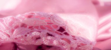 Şatafatlı saten kumaşın üzerine yayılmış karmaşık pembe dantelli bulanıklık, ince dantel dokular ve pürüzsüz saten kıvrımların karışımı lüks, kadınsı bir görünüm yaratıyor..