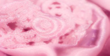 Pembe dantelli kumaşın yakın plan görüntüsü. Çiçek desenleri pürüzsüz saten üzerine örtülmüş. Doku ve renk, moda ve dekorasyon için yumuşak ve lüks bir estetik oluşturuyor.