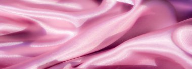 Pürüzsüz pembe saten kumaştan bulanık, parlak detaylar. Kumaş nazikçe akar, yumuşak kıvrımlarla zarif ve lüks bir görünüm yaratır. Yüzeyde ışık parıldıyor,