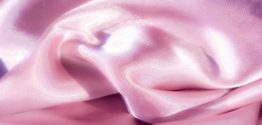 Pürüzsüz pembe saten kumaştan bulanık, parlak detaylar. Kumaş nazikçe akar, yumuşak kıvrımlarla zarif ve lüks bir görünüm yaratır. Yüzeyde ışık parıldıyor,