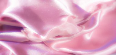 Bulanık, parlak bir dokusu olan yumuşak pembe saten kumaşın yakın plan görüntüsü. Işık, kumaşın pürüzsüz ve akışkan kıvrımlarını vurguluyor.