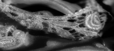 Nazik kıvrımlar halinde akan yumuşak, parlak bir kumaşın yakın plan çekimi. Pürüzsüz yüzey ışığı yansıtır, derinlik yaratır ve gri tonda lüks bir görünüm yaratır..