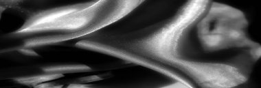 Derin kıvrımları ve yumuşak dokusu olan saten kumaştan siyah bir Blur. Işık parlak maddeyi yansıtıyor, gölgeler ve gölgeler arasında zarif bir etkileşim yaratıyor, lüks hissi arttırıyor.