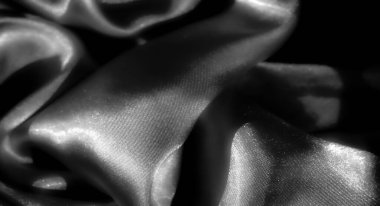 Yumuşak dokuları ve dalgalı kıvrımları olan siyah kumaş bulanıklığı. Işık, satenin yüzeyinde dans eder, güzel bir parıltı ve gölgeler ve gölgeler arasında kontrast oluşturur.