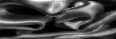 Pürüzsüz, parlak bir yüzeye sahip siyah bulanık kumaş kıvrımları ışık ve gölgelerin hassas etkileşimini yakalıyor. Monokrom estetiği sonsuz, sofistike bir his katar.