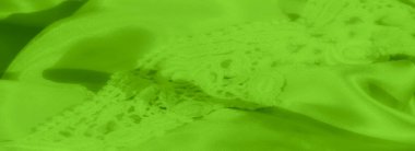 Pürüzsüz, parlak yeşil saten kumaşın karmaşık dantel kaplamalı bulanık görüntüsü. Saten 'in parlak yüzeyi, her iki materyalin ince detaylarını ortaya çıkaran dokulu dantelle çelişiyor.