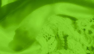 Parlak yeşil saten ve dantel kumaştan bulanık bir yakın plan, pürüzsüz, katlanmış saten yüzey üzerindeki karmaşık dantel tasarımı vurguluyor. Kumaşın dokusu ve parlaklığı çok güzel.