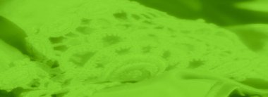 Canlı yeşil bir dantelin bulanıklığı ve karmaşık detaylarıyla kumaş tekstili. Yumuşak kıvrımlar hassas dantel desenine kusursuz bir şekilde karışır, yumuşak ve zarif bir doku yaratır.