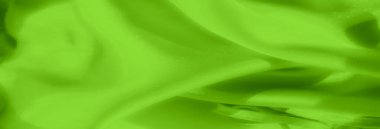 Yumuşak kıvrımlı canlı yeşil saten kumaştan bulanık, yumuşak yansımalı pürüzsüz, parlak bir yüzey yaratıyor, maddenin lüks ve ipeksi doğasını sergiliyor..
