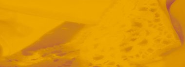 Detaylı çiçek desenlerini ve yumuşak dokuyu vurgulayan sarı dantelli kumaşın bulanık görüntüsü, tasarım projeleri veya dekor temaları için konforlu ve karmaşık bir tekstil arkaplanı oluşturur.