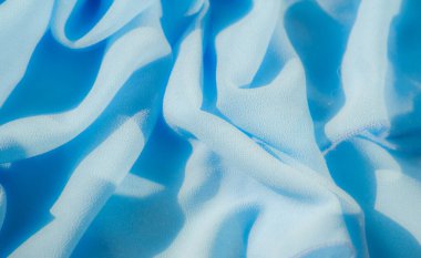 Görüntü. Açık mavi kumaş. Karmaşık kıvrımları ve yumuşak dokuları var. Materyalin hareketini ve akışkanlığını güzel bir şekilde yakalıyor. Yumuşak ışık ince gölgeler yaratır.