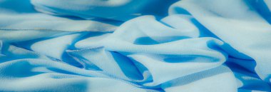 Görüntü. Yumuşak dalgaları ve pürüzsüz kıvrımları olan canlı, açık mavi bir kumaş. Dokulu yüzey ışıkla zarif bir şekilde etkileşime girer ve zarif bir ışık yaratır.