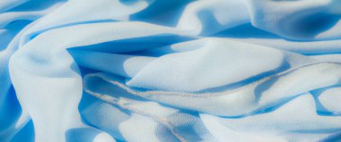 Görüntü. Yumuşak kıvrımlı ve desenli yüzeyi olan açık mavi bir kumaş, yumuşak bir akış ve pürüzsüz bir görünüm yaratıyor. Işık ve gölgenin etkileşimi kumaşın hassas dokusunu güçlendirir.