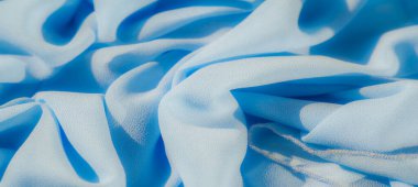 Açık mavi kumaş bulanıklığı yumuşak dalgalar halinde güzelce katlanmış. Yumuşak doku ve dingin renk paleti, yumuşak kırışıklıkları ve ışık etkileşimini vurgulayarak rahatlatıcı bir görsel etki yaratır..