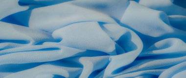 Yumuşak kıvrımlarla örtülmüş açık mavi kumaş. Yumuşak ve pelüş dokusu, maddenin doğal akışını ve pürüzsüzlüğünü vurgulayan huzurlu ve dingin bir estetik yaratıyor..