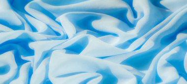 Görüntü, yumuşak mavi kumaş kıvrımlarını bulanıklaştırarak yumuşak ve dingin bir doku oluşturuyor. Malzeme gölgeler ve gölgelerle pürüzsüz bir şekilde akıyor, rahatlatıcı bir estetik sunuyor..