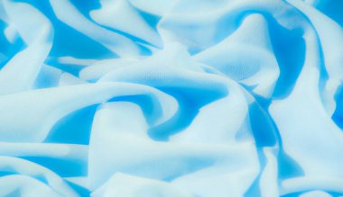 Yumuşak mavi tekstil dalgalar halinde dalgalanır. Kumaşların hassas dokusu ve pürüzsüz kıvrımları, sakin ve minimalist arkaplanlar için ideal soyut bir tasarım yaratıyor..