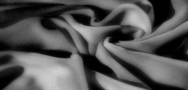 Siyah, gri tonda kıvrımlı dalgalı kumaşlar. Yumuşak dokuyu pürüzsüz bir çizgi akışıyla gösteriyor. Aydınlık ve karanlık tonlar arasındaki oyun minimalist bir estetik ile büyüleyici bir görsel yaratıyor..