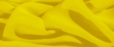 Yumuşak sarı kumaşın bulanık kıvrımları soyut bir tasarım ile nazik dalgalar oluşturur. Yumuşak doku ve parlak renk, maddenin hassas ve akıcı doğasını vurgulayan yumuşak ışıkla aydınlatılır.