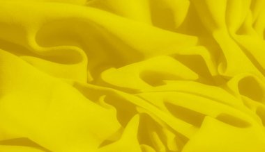 Pürüzsüz, dalgalı kıvrımları olan sarı kumaşın bulanık görüntüsü. Yumuşak madde ışığı yakalar, kumaşa narin ve dalgalı dokusunu vurgulayan aydınlık, ışıl ışıl bir görünüm verir..