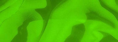 Canlı yeşil kumaştan bulanık, yumuşak kıvrımlı ve narin yüzeyi var. Malzeme, dokunsal kaliteyi vurgulayarak gölgeler ve röflelerle dinamik bir akış yaratıyor..