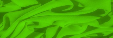 Yumuşak dalgalanmalar ve pürüzsüz dokularla kaplı parlak yeşil kumaştan oluşan bulanık bir görüntü, hafif röfleler ve gölgelerle dinamik, akıcı bir form yaratarak, maddenin esnekliğini vurguluyor..