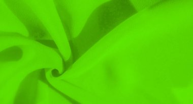 Yeşil kumaşın bulanık görüntüsü yumuşak ve dalgalı kıvrımlar oluşturuyor. Katlar, yüzey boyunca yumuşatıcı ve akıcı bir hareket yaratarak kumaşın dokusunu vurguluyor..