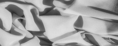 Nazikçe katlanmış gri kumaş bulanıklığı, ışık ve gölge oyunu. Yakın çekim, materyalin yumuşak dokusunu ve organik akışını vurgular, barışçıl ve sanatsal bir görsel sunar..