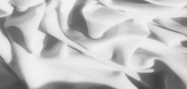 Yumuşak gri kumaş kıvrımları karmaşık detaylar içinde yakalanmış. Doku pürüzsüz ama hafif kumlu bir görüntü yaratıyor. Kumaşın kıvrımlarında gölgeler soyut desenler oluşturuyor..