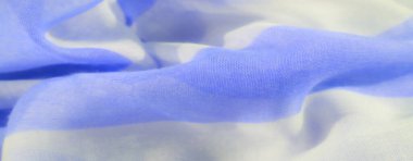 Beyaz ve mavi çizgili hafif bir kumaşın bulanık yakın çekimi. Katlar yumuşak bir akış yaratıyor. Işığı yansıtan yumuşak bir yüzey. Havadar ve narin doğasını vurguluyor..