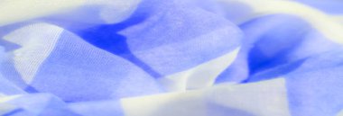Açık mavi ve beyaz kumaşın ince kıvrımlı bulanık görüntüsü. Kumaş yumuşak, pürüzsüz bir dokuyu sergiliyor, maddeden yansıyan ışıkla, saf ve zarif bir his yaratıyor.
