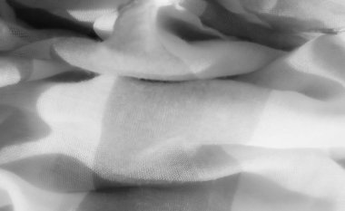 Açık gri ve beyaz desenli bulanık kumaş, karmaşık kıvrımları ve kıvrımları olan yumuşak bir doku, soyut ve dingin bir kumaş akışı sunar..