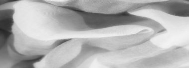 Görünür kıvrımlarla yumuşak ve havadar bir dokuyu gösteren gri pullu kumaşın bulanık yakın çekimi. Malzemenin ışık şeffaflığı, tek renkli palette akan ve nazik şeklini vurgular..