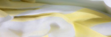 Katlanmış sarı ve beyaz kumaş bulanıklığı yumuşak ve narin bir doku oluşturuyor. Yumuşak kıvrımlar ve kumaştaki nazik dalgalar bir sakinlik hissi uyandırıyor, ışıkların nazikçe yansımasıyla güçleniyor.