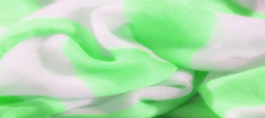 Hassas, açık yeşil ve beyaz kumaşlar birbirine dolanmış, pürüzsüz, akışkan desenler oluşturuyorlar. Renklerin yumuşak dokusu ve kusursuz karışımı dinamik bir tekstil tasarımı yaratır.