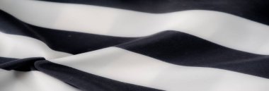 Yumuşak siyah ve beyaz çizgili kumaşın bulanık görüntüsü yumuşak kıvrımlarda akıyor. Açık ve koyu çizgiler arasındaki pürüzsüz doku ve güçlü kontrast zarif ve modern bir tekstil tasarımı yaratır..