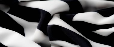 Yumuşak kıvrımları ve gölgeleri olan pürüzsüz siyah ve beyaz çizgili kumaş. Alternatif çizgilerin karşıtlığı dinamik bir görsel etki yaratarak, kumaşın yüzeyinin dokusunu vurguluyor..