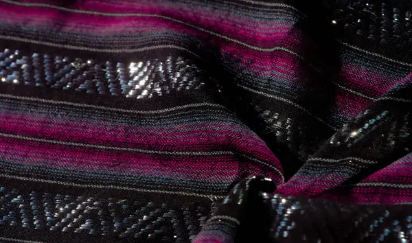 Parlak pembe ve mavi çizgili siyah kumaş kalın bir yapı oluşturur. Tekstil katları ve dokuma elementleri yansıyan ışık tarafından vurgulanarak derinlik ve detay eklenir.