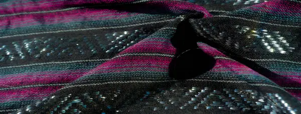 Kumaşın karmaşık siyah, morumsu ve mavi dokumasını bulanıklaştırır. Dokuma yüzeyinde parıldayan parlak renkler görünür. Renk kontrastı kumaşın zengin detaylarını geliştirir.