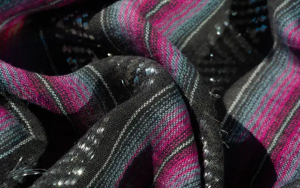 Koyu pembe ve turkuaz çizgili desenli siyah kumaş. Buruşuk yüzey derinlik ve görsel ilgi ekliyor. İnce parıltılı detaylar materyale yayılıyor..