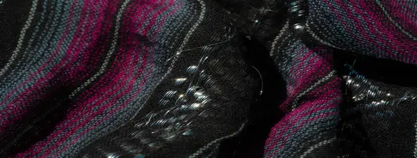 Koyu pembe ve turkuaz çizgili desenli siyah kumaş. Buruşuk yüzey derinlik ve görsel ilgi ekliyor. İnce parıltılı detaylar materyale yayılıyor..