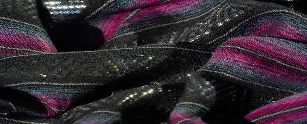 Koyu pembe ve turkuaz çizgili desenli siyah kumaş. Buruşuk yüzey derinlik ve görsel ilgi ekliyor. İnce parıltılı detaylar materyale yayılıyor..