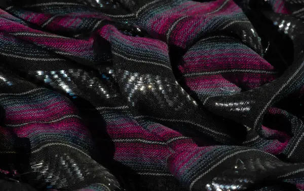 Pembe ve mavi dokuma aksanlı lüks siyah kumaş, ışığı yakalayan parlak gölgeler ve lüks tekstil için mükemmel, çarpıcı bir görsel doku yaratıyor..
