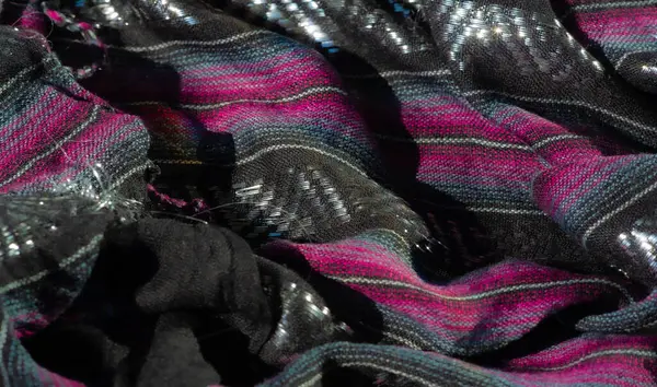 Karmaşık siyah, pembe ve mavi çizgili, parlak ipliklerle güçlendirilmiş bulanık kumaş. Dokulu yüzey ışığı yansıtır, dinamik ve görsel olarak çarpıcı bir bileşim yaratır.