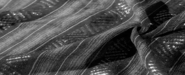 Dokulu çizgileri ve parıldayan geometrik şekilleri olan siyah kumaşın bulanık görüntüsü. Kumaşın üzerindeki ışık oyunu detaylı tasarıma zarif ve modern bir dokunuş ekler..