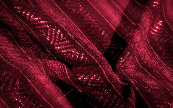 Parlak dokuma elementleri ve yansıtıcı röfleleri olan zengin kırmızı kumaştan bir bulanıklık. Karmaşık desenler ve derin tonlar görsel olarak büyüleyici ve lüks bir doku yaratıyor.