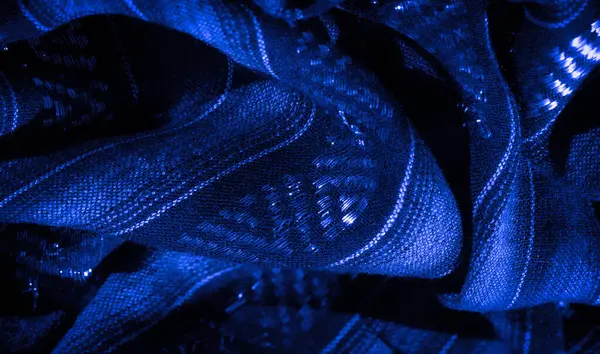 Pürüzsüz bir akış ve karmaşık desenler sunan parıldayan parlak ışıklarla, dokulu mavi kumaşın bulanık görüntüsü. Zengin mavi tonlar büyüleyici bir görsel cazibe yaratır..